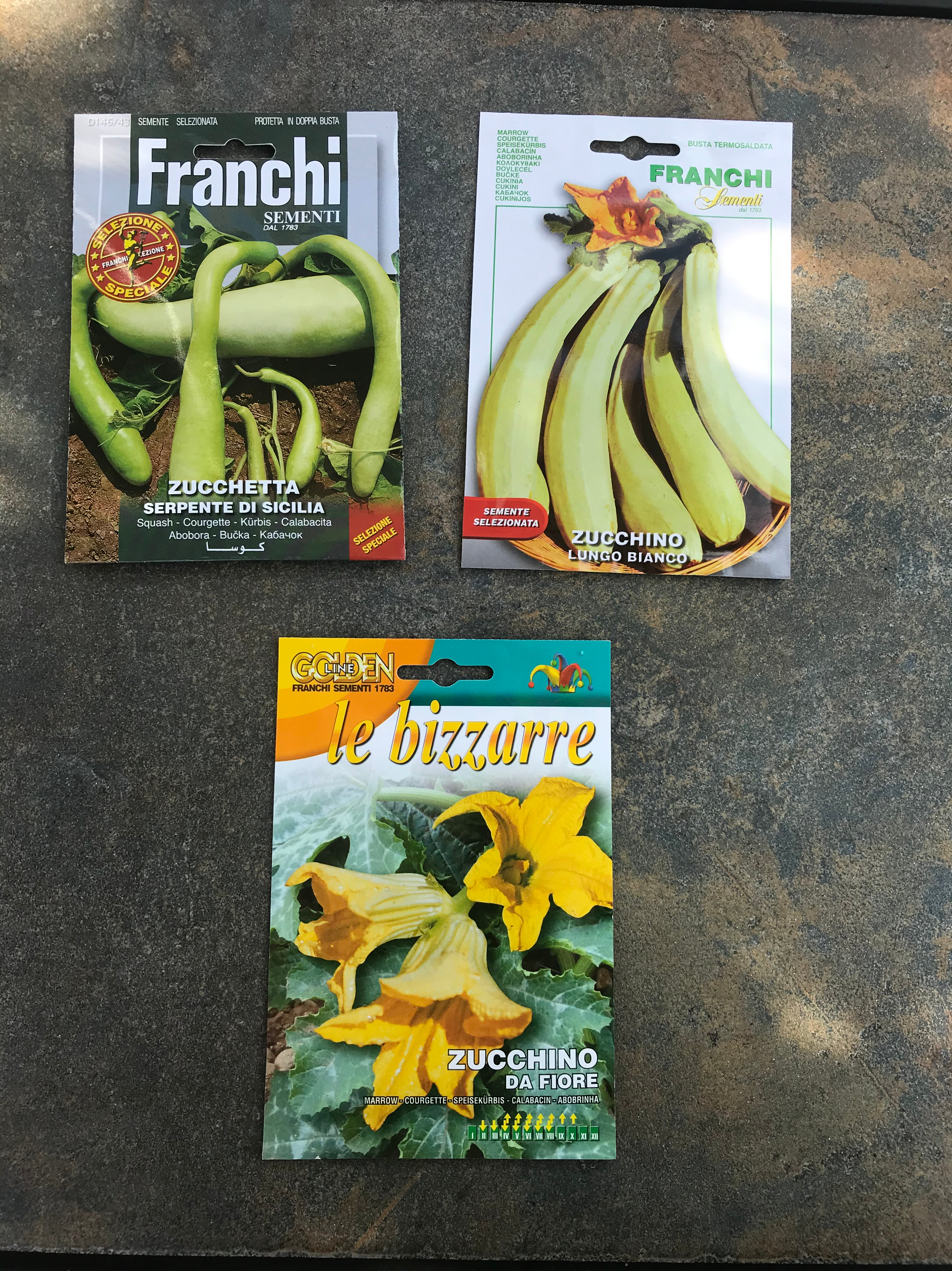 Three seed packets with pictures of different types of zucchini.