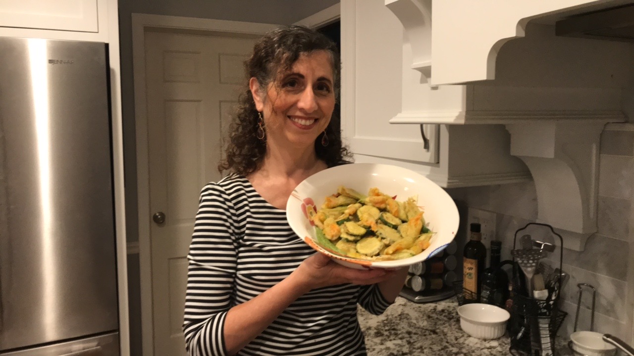The author in her kitchen holding a bowl of fried zucchini flowers ad fried zucchini rounds