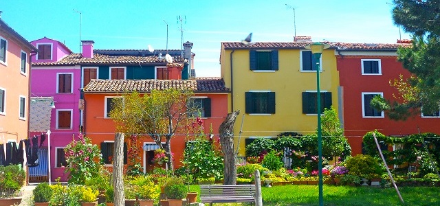 Colorful homes on a block in Burano with a garden and a park bench out front